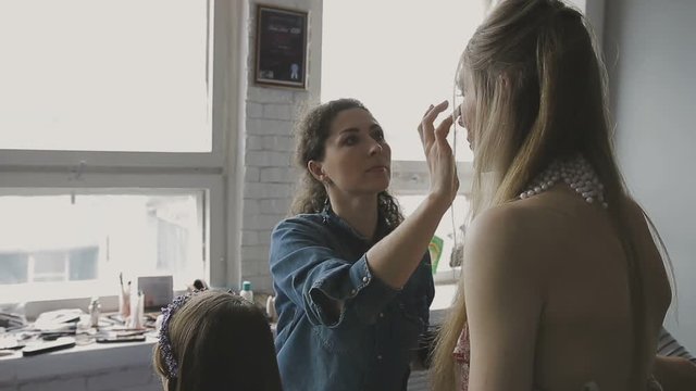 Make-up artist makes a professional make-up for a very beautiful girl in a photo studio