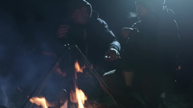 Night shot of two caucasian friends have a discussion next to campfire.