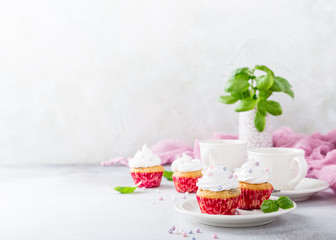 Mini cupcakes with white frosting cream and pink sprinkles on light gray background. Decorated with basil leaves. Party food concept. Copy space.