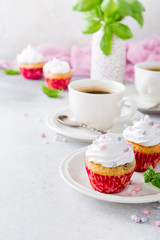 Mini cupcakes with white frosting cream and pink sprinkles on light gray background. Decorated with basil leaves. Party food concept. Copy space.