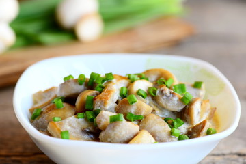 Mushrooms slices in a sour cream sauce. Mushrooms stewed with sour cream and green onions in a bowl. Healthy vegetarian snack recipe. Vintage wooden table. Closeup