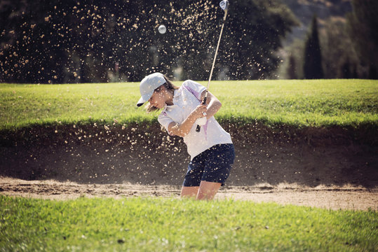 young girl playing golf on a sunny day moving sand in the banker