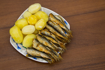 Fried baltic herring with boiled potatoes on a plate on wooden background