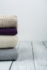 Knitted wool sweaters. Pile of knitted winter clothes on wooden background, sweaters, knitwear, space for text.