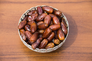 Dates fruit on a silver bowl on wooden table. The Muslim feast of the holy month of Ramadan Kareem