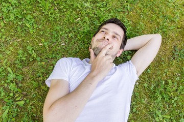 Young happy man is lying on green grass and thinking or dreaming.