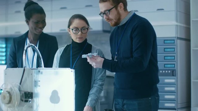 Three Very Bright and Young Multiethnic Students Discussing 3D Printed Mechanism in a New Modern Laboratory. Shot on RED EPIC-W 8K Helium Cinema Camera.