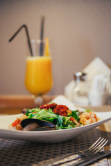 Seafood salad on the table in the cafe. Orange freshly squeezed juice on the background. indoor. Knife and fork near the plate