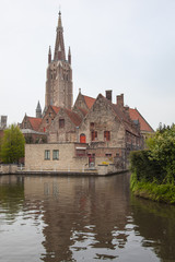 Fototapeta premium View of Minnewater pond with historical red brick buildings and the tower of the Church of Our Lady in spring in the medieval neighborhood of Bruges (Brugge), Belgium