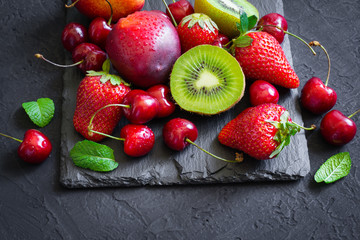 Assorted of Juicy summer fruits and berries. Strawberry, cherry, kiwi and peaches on black slate...