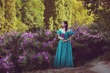 Fototapeta na wymiar Young woman in lush bushes of lilac, she sadly dreams.