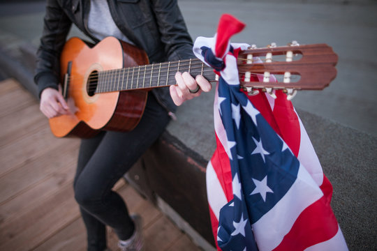Artist with the US flag playing the guitar. Acoustic concert on the roof. Unrecognizable teenager on vacation at a party on Independence Day