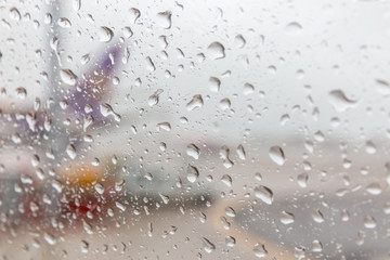 Blurred photo of rain drops on airplane window glass and blurred airport runway in background.