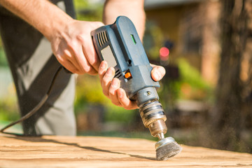 Hands man with electrical rotating brush metal disk sanding a piece of wood