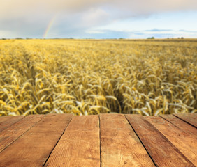 wood table and blurry Field with mature cereal ears and rainbow in background. Empty table for display product.