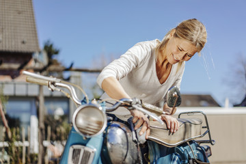 Smiling woman cleaning vintage motorcycle