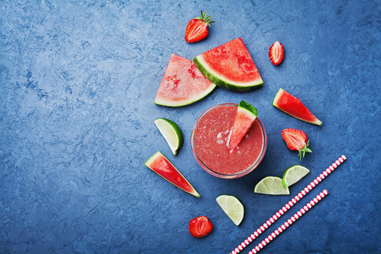 Tropical watermelon smoothie with slices of fruit on blue background top view in flat lay style. Summer detox juice.