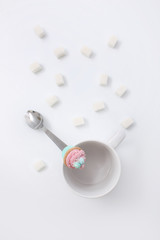 White cup with cubes of sugar and a spoon with a cake on a white background
