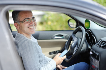 Smiling man in a car with smartphone in the hand