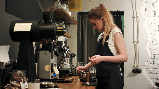 Pretty young female barista weighing coffee grains on a scale before brewing a cup of coffee