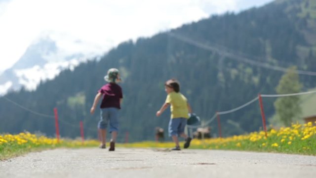Happy children walking on a rural path in Swiss Alps, springtime, cows in the field