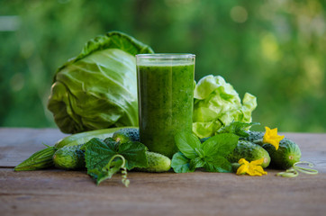 Green smoothie with cucumber, mint, zucchini and cabbage as healthy summer drink isolated on wooden table