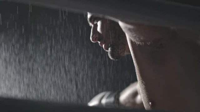 Handheld shot with close up of tired boxer resting in his corner in between rounds and being sprayed with water to cool down