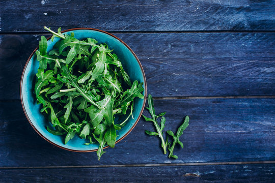 Fresh arugula leaves in plate. Green vegan salad on a blue wooden table background. Top view, copy space