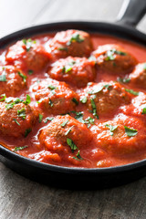 Meatballs with tomato sauce in iron frying pan on wooden table. 
