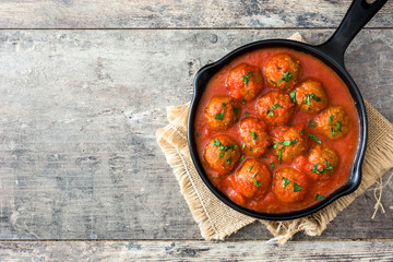 Meatballs with tomato sauce in iron frying pan on wooden table. Top view