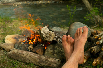 the legs of a man warming themselves by the campfire outdoors