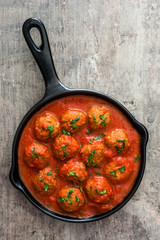 Meatballs with tomato sauce in iron frying pan on wooden table. Top view