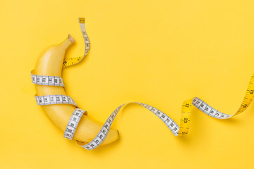 Diet, fitness and health concept presented by yellow banana wrapped in measure tape isolated on yellow paper background © makistock