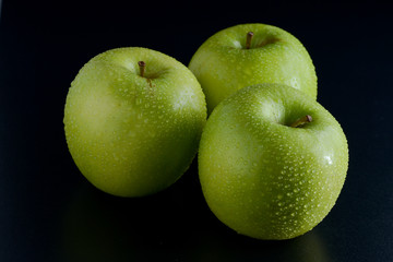Three green apples with droplets on black background