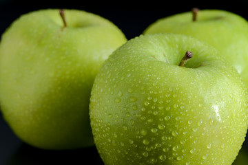 Green apples with droplets on black background