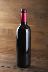 Vertical studio shot of unlabeled red wine bottle placed on wooden table.