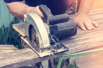 Male hand cuts with a circular saw a piece of Board on a Sunny day, close-up. Toned.
