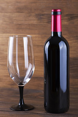 Red wine bottle and a glass placed on wooden table. Copy space. Vertical studio shot