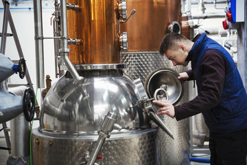Man looking into a metal tank in a distillery.