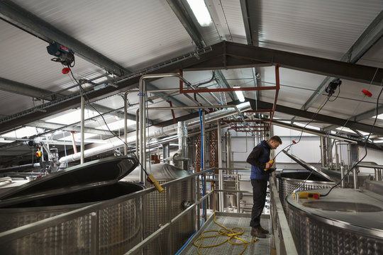 Man checking large metal tanks in a distillery or brewery, lifting the lid on a chamber full of beer mash.