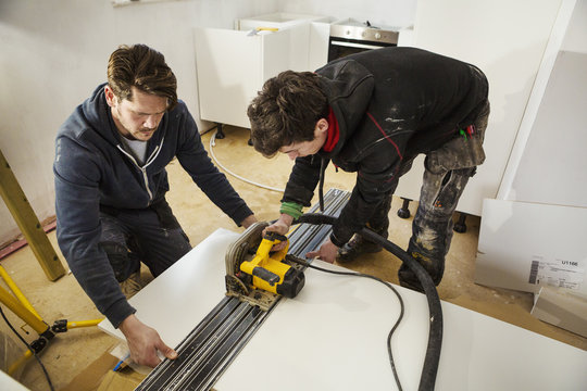 Two builders, cutting plasterboard with a circular saw.