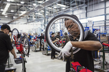Male skilled factory worker assembling a bicycle in a factory, attaching a wheel.