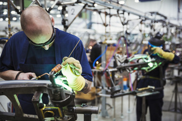 Male skilled factory worker using welding tools on a bicycle frame in a factory.