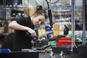 A young woman using a power tool, a skilled factory worker assembling cycle parts.