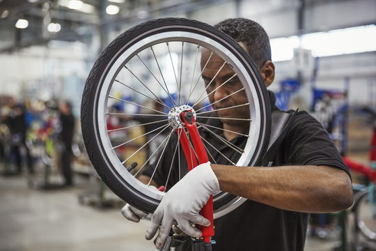 Male skilled factory worker assembling a bicycle in a factory, attaching a wheel.