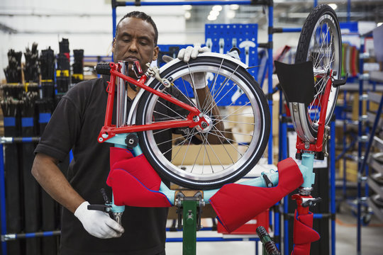 Male skilled factory worker assembling a bicycle in a factory, attaching a wheel.
