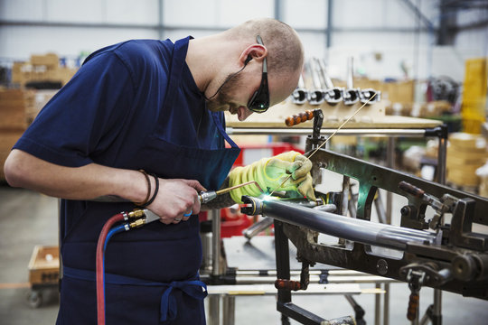 Male skilled factory worker welding parts of a bicycle in a factory.