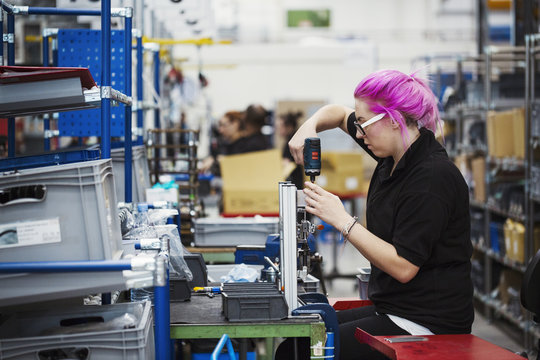 A young woman with pink hair using a power tool on a cycle frame.  A skilled factory worker assembling a bicycle in a factory.