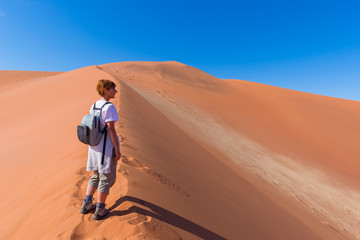Fototapeta na wymiar Tourist walking on the scenic dunes of Sossusvlei, Namib desert, Namib Naukluft National Park, Namibia. Adventure and exploration in Africa.