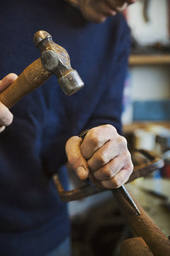 Man standing in a workshop, holding a hammer and wood chisel, working on a piece of wood.